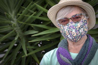 Close-up portrait of senior woman wearing mask sitting against plant