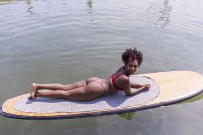 High angle portrait of young woman wearing bikini while lying on paddleboard in lake