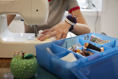 Midsection of tailor using sewing machine by blue box at table