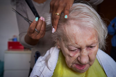 Caring african american woman caregiver, cutting her elderly woman hair at home