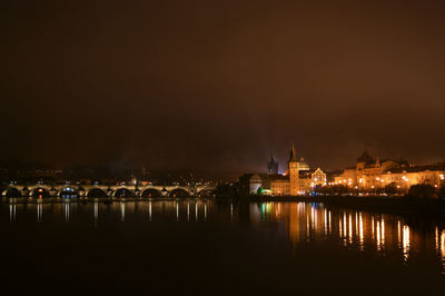 Illuminated city by river against sky at night