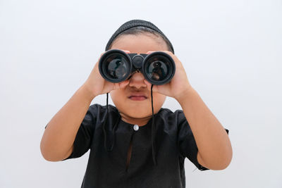 Portrait of boy looking through binoculars against white background