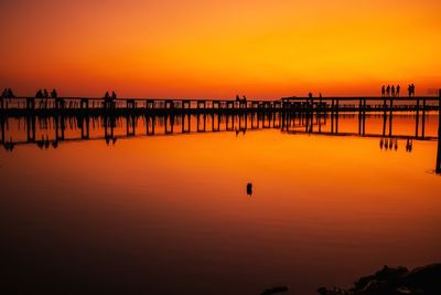 Silhouette pier on sea against orange sky