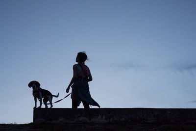 Low angle view of man and dog walking against clear sky