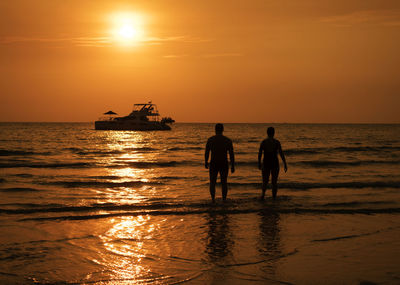 Silhouette people standing in sea against sky during sunset