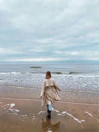 Rear view of woman standing at beach against sea and sky