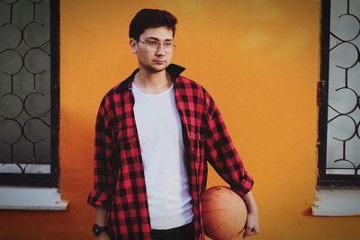 Young man with ball standing against wall