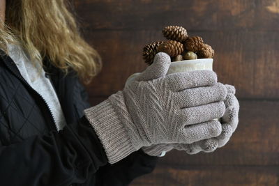 Midsection of woman holding coffee cup with pine cone at home