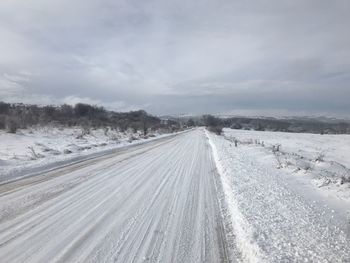 Tire tracks on road against sky during winter