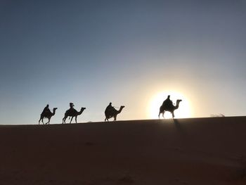 Silhouette people walking on desert against clear sky