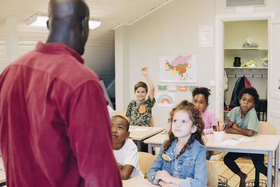 Rear view of male teacher teaching students in classroom