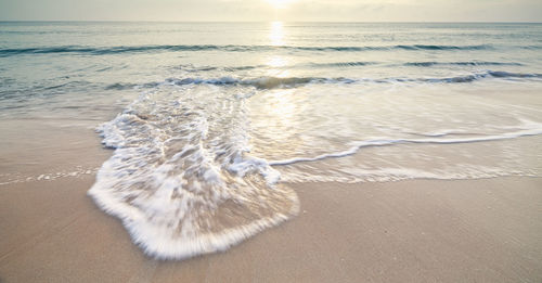 Long exposure shot sandy beach and the sea wave white bubbles with the sunrise background 