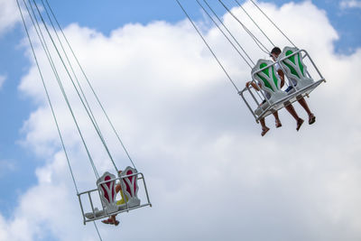 Low angle view of people sitting on amusement park ride against cloudy sky