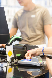 Hands of female customer paying through credit card at checkout with cashier in store