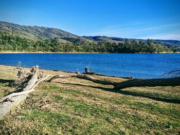 Scenic view of lake  mountains and fisherman against blue sky