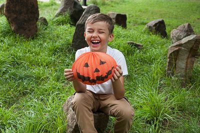 Smiling boy holding jack o lantern sitting on field