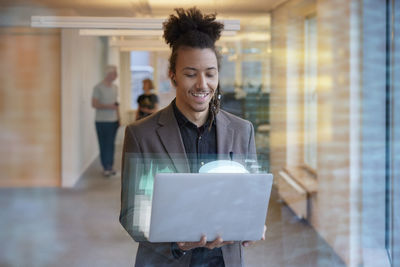 Young businessman holding laptop in office corridor