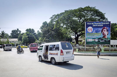 Cars on road by trees against sky in city