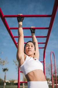 Female athlete exercising on monkey bars in public park on sunny day