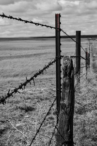 Close-up of barbed wire on wooden post against sky