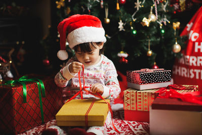 Cute girl opening christmas present against tree at home