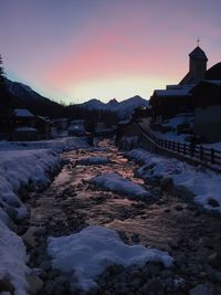 Snow covered buildings in city against sky during sunset