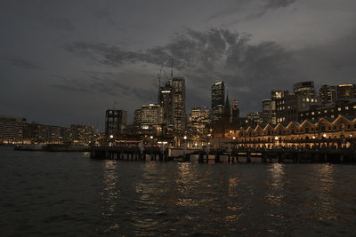 Illuminated buildings by river against sky at night