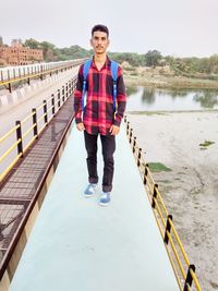 Portrait of young man standing on railing by lake