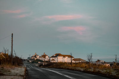 Road by buildings against sky