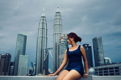 Woman sitting on retaining wall against petronas towers