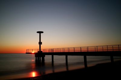 Silhouette railing by sea against clear sky during sunset