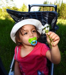 Cute girl holding flowers while sitting in stroller at park