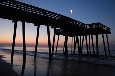 Low angle view of illuminated windsock on pier at beach during sunset