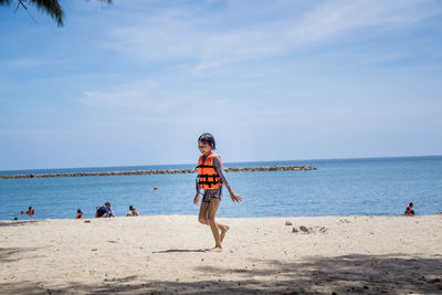 Smiling girl walking at beach against sky