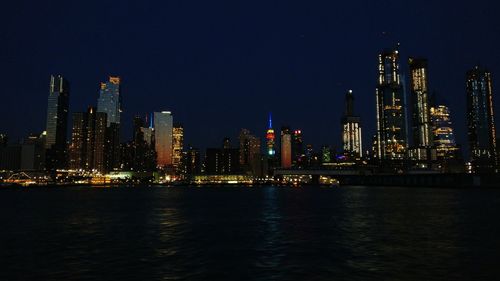 Illuminated buildings by river against sky at night