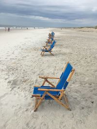 Deck chairs on sand at beach against sky