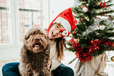 Portrait of young woman with dog on christmas tree