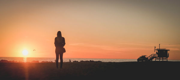 Silhouette woman standing on beach against sky during sunset