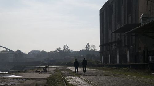 Two people walking on road along building