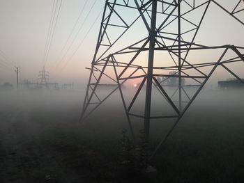 Electricity pylon on landscape against sky during foggy weather