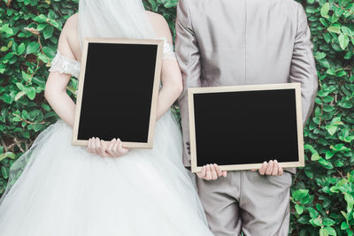 Rear view of bride and bridegroom holding blank slates