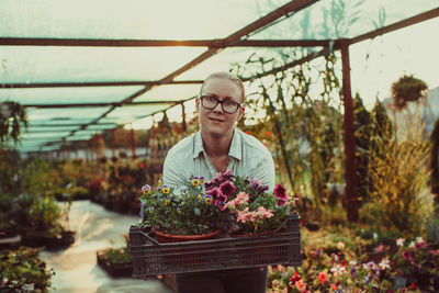 Portrait of smiling woman standing by plants at greenhouse