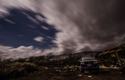 Abandoned car on field against storm clouds