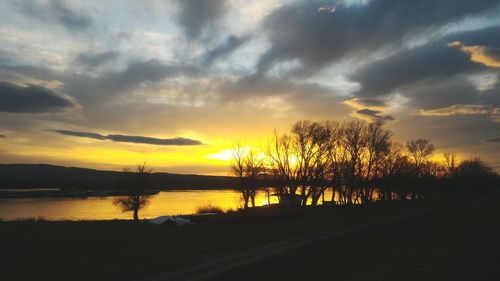 Silhouette trees on landscape against dramatic sky during sunset