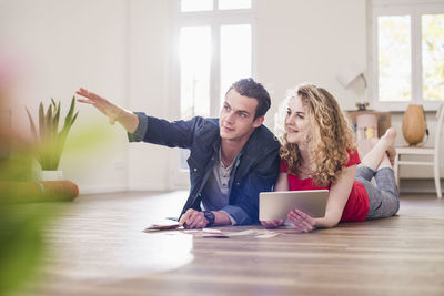 Young couple in new home lying on floor with tablet choosing from color sample