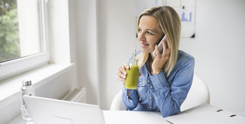 Young woman using phone while sitting on table