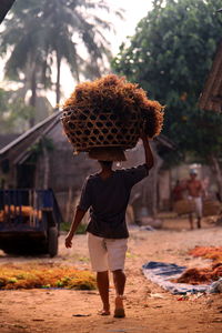 Full length rear view of man carrying wicket basket in village