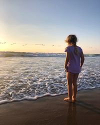 Rear view of girl standing on beach against sky