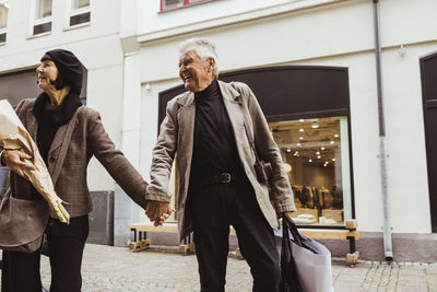 Smiling senior man holding hands of woman while walking on street in city