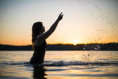 Beautiful russian girl in a long black swimsuit swims outside the city on the lake.